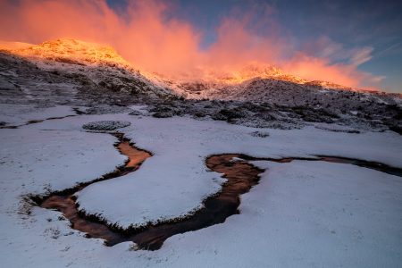 una montaña cubierta de nieve con un arroyo que la atraviesa